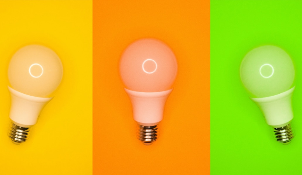 Drei verschiedenfarbige Glühbirnen auf buntem Hintergrund (gelb, orange, grün). Ein lebendiges Bild voller Farben und Licht.